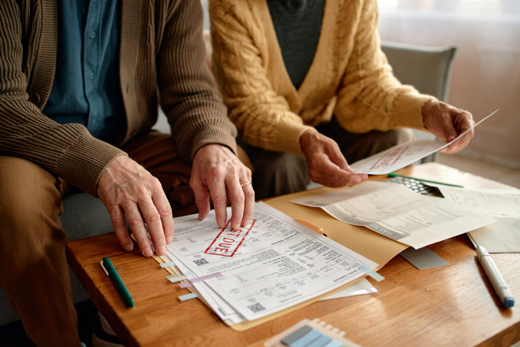 A senior couple examines overdue utility bills at home, stressing the financial need for better energy efficiency solutions.