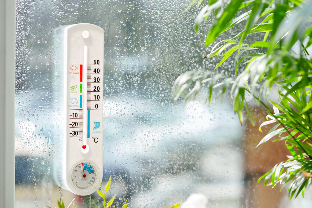Indoor humidity levels measured with a hygrometer beside a window showing moisture and condensation